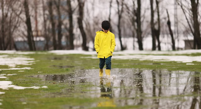 Boy playing in the rain, wearing boots and raincoat