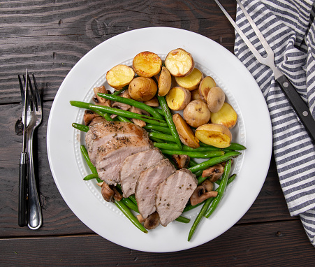 overhead angle of pork loin filet over roasted green beans with utensils