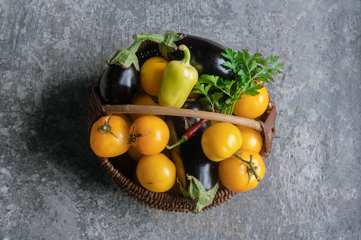 Fresh vegetables in a wicker basket on a stump with black background and copy space.