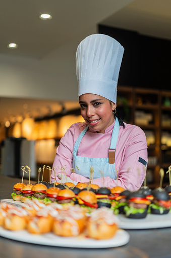 Latina woman of average age 30 years old dressed in uniform and chef's hat is in the kitchen of a beautiful restaurant preparing delicious platinum dishes that will be enjoyed by her diners.