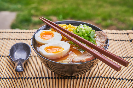 Japanese style udon or ramen soup made from pork broth and pork meat, noodles, soft boiled egg and vegetables and served in traditional bowl with spoon and chopsticks. Delicious and satisfying lunch.