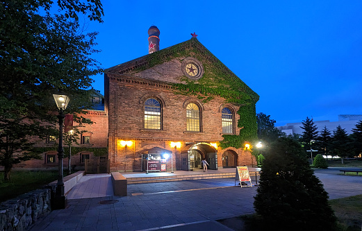 Sapporo, Japan - May 29, 2023: Outside the historic Sapporo Beer Museum and Sapporo Beer Garden during spring twilight. The modern Ario Sapporo shopping mall stands in the background.