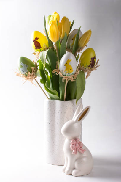 istock Easter table setting, painted eggs with a bouquet of yellow tulips and an Easter bunny. Greeting card 2100111663