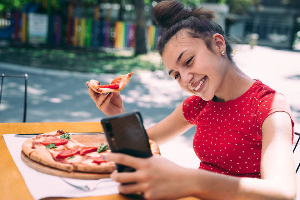 istock Teenager eating pizza looking in phone. Using phone. 2100152981