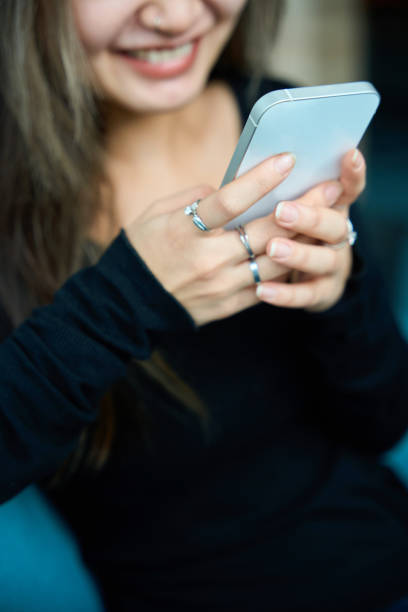 Focus on foreground of smartphone using cropped blurred young smiling asian woman. Concept of modern freelance or remote work