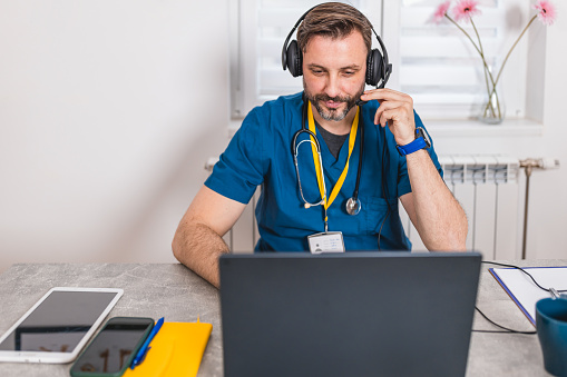 From his office, a male nurse conducts a telehealth session using his laptop and headphones, demonstrating the effectiveness of remote patient care