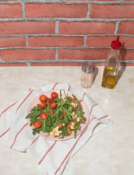 Harvested arugula, cherry tomatoes, almond, cashew on a pink plate in a kitchen marble table. Food ingredients concept