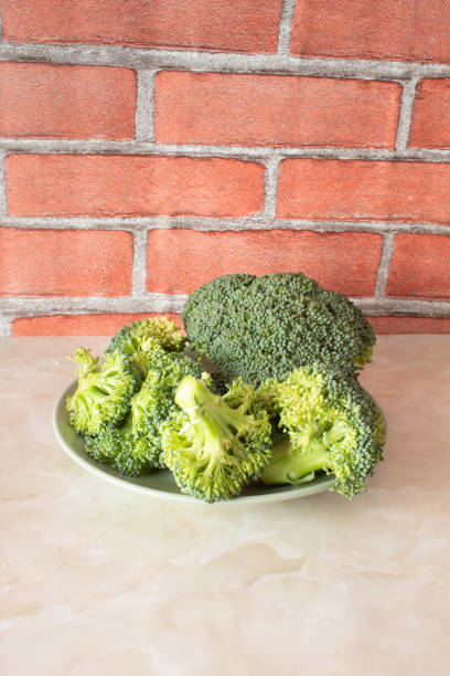 Broccoli is placed on a surface with natural light shining on it. The green vegetable is ready for washing and cooking in a kitchen.