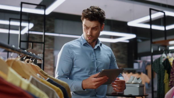istock Boutique worker walking clothes rows checking tablet in clothing store closeup 2100303820