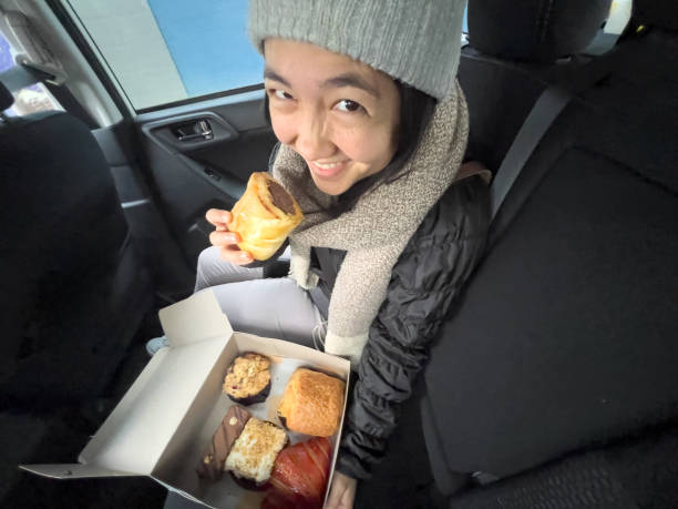 Multiracial Woman in Car Eating Vegan Sausage Roll from Bakery