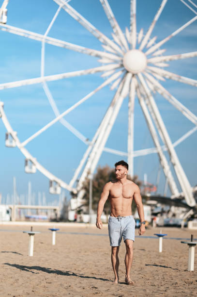 młody wysportowany mężczyzna spacerujący boso po plaży. - men swimwear full length fashion model zdjęcia i obrazy z banku zdjęć