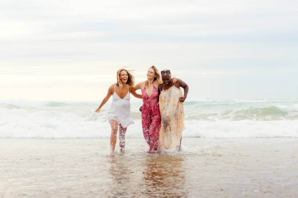 Multiracial female group of three friends holding together, cooling off in the sea water and enjoying a summer day at the beach. Friendship, unity and diversity