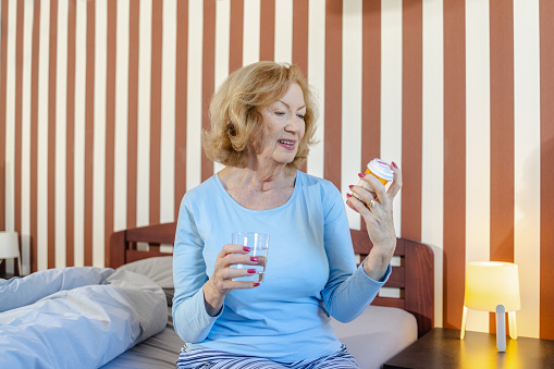 Photo of beautiful senior woman in pajamas holding medicines bottle