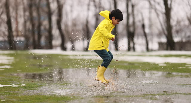 Boy playing in the rain, wearing boots and raincoat