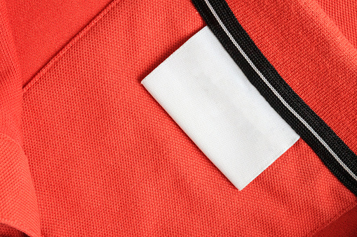 Blank white laundry care clothes label on orange shirt fabric texture background