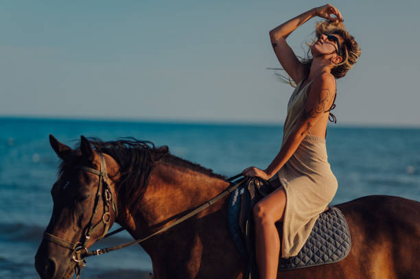 istock A tattooed lady is horseback riding on a beach at sunset. 2100390389