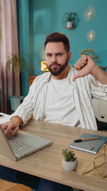 Upset business man freelancer working on laptop showing thumbs down sign disapproval dissatisfied