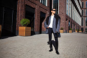 Stylish fashion woman strolls down the street in an oversized blazer, black leggings, and knee high rubber boots. Fashionable outfit, street style