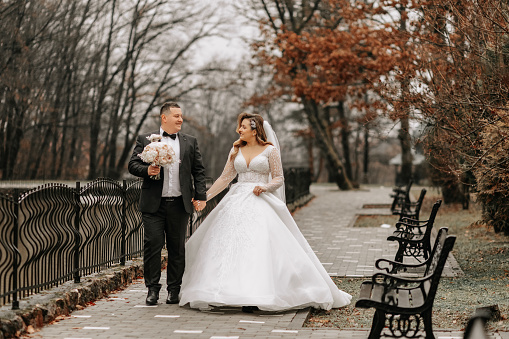 The bride and groom are walking near the hotel and posing, happy and enjoying the day, holding hands. A long train on the dress. Winter wedding