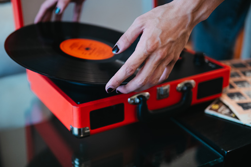 A detailed view of a hand placing a black vinyl record on a vibrant red portable turntable