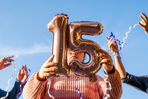 Girl holding 15th birthday balloons in party outdoors