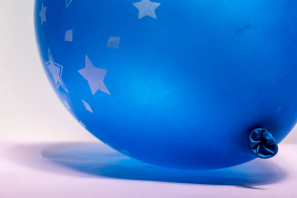 Cropped hand of young woman holding blue balloon against yellow background