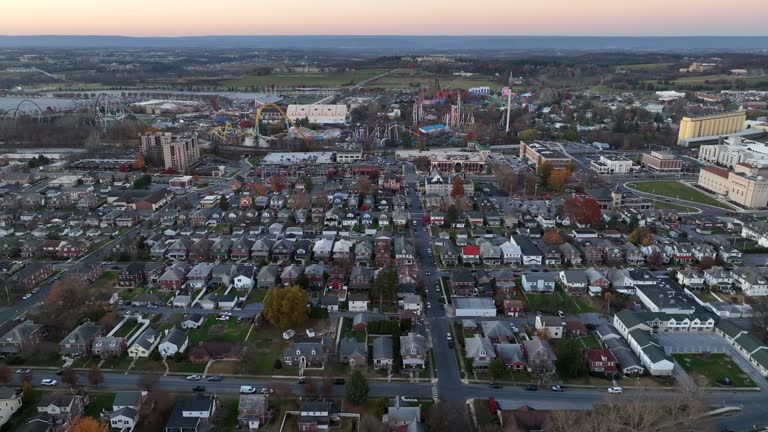 Wide aerial of Hershey, Pennsylvania during autumn sunset. Quaint small town neighborhood with Hershey Park and chocolate factory in distance at dusk.