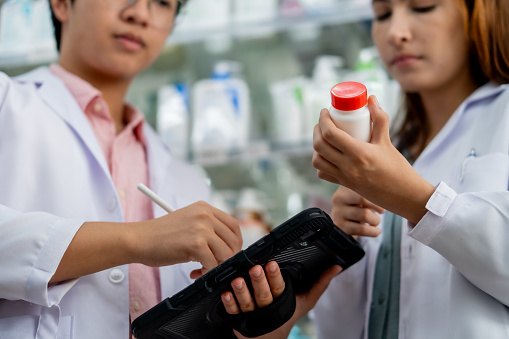 Two attentive pharmacists use smartphones to search for information about medicine bottles in a pharmacy.