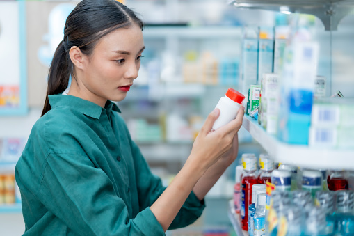 A female pharmacist working in a pharmacy or chemical store is checking the stock and checking the expiration date of medicines in the store.