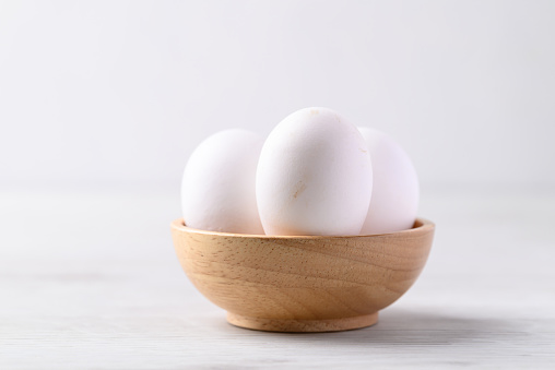 Organic white leghorn egg from free range farm in wooden bowl on white table
