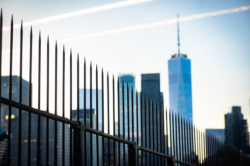 This is a photograph with a selective focus of a sharp fence in the foreground with a defocused New York City skyline including the Freedom Tower.