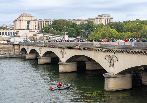 Firefighter with a neoprene suit in an inflatable boat in front of a bridge on the Seine River. Paris. France. August 5, 2023.