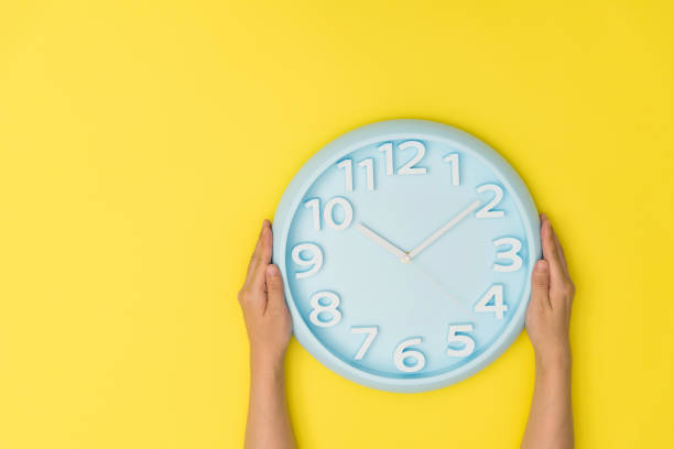 human hand holding a clock on yellow background - clock time clock hand urgency foto e immagini stock