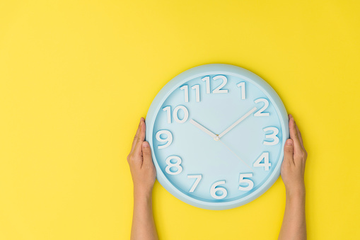 Human hand holding a clock on yellow background.