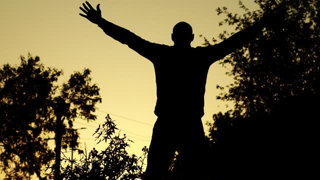 Silhouette of young man hand raised in the nature