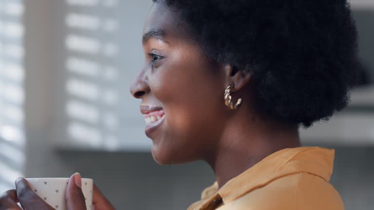 Side view of woman drinking coffee in morning and looking out window.