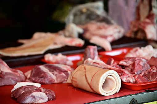 A close-up shot at a market pork stall captures the bundled pigskin with rubber bands. Nearby, various pork products like pork and ribs are displayed.