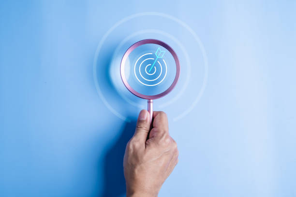 istock hand holding target board inside magnifying glass for focus business. search, goal, strategy. 2100815178