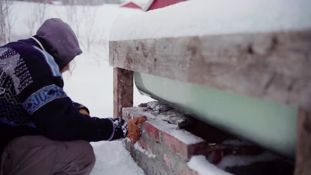 The Man is Brushing Snow Off the Bricks and Placing Them Beneath the DIY Hot Tub - Close Up