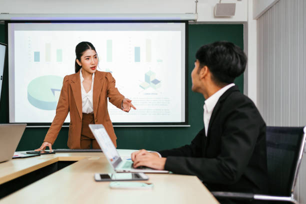 istock A cheerful and confident Asian businesswoman stands, present bar charts data from projector screen to her office colleagues. Asian business women leader role at the meeting. 2100866621