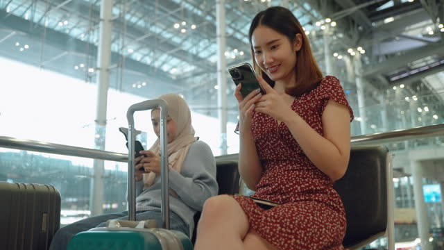 The Asian female tourist is sitting, waiting for her flight within the airport, reflecting the concepts of tourism, travel, and business travel.