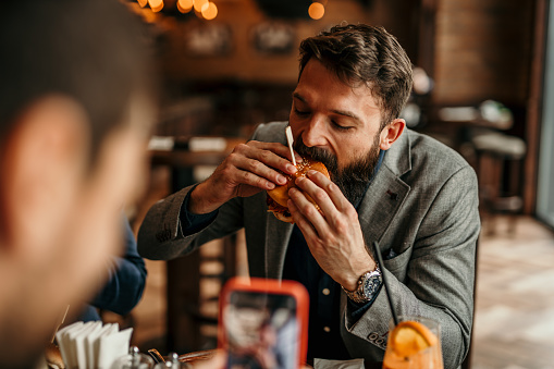 Two businessmen taking a photos while dining burgers at a restaurant