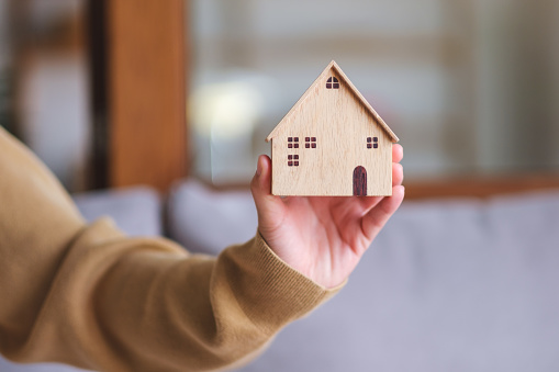 Closeup image of a woman holding and showing a wooden house model
