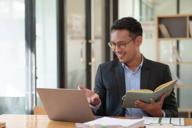 istock Smiling asian businessman with a notebook giving an online presentation. Professional webinar and virtual meeting concept. 2101006281