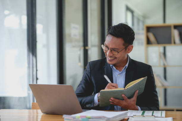 istock Smiling asian businessman with a notebook giving an online presentation. Professional webinar and virtual meeting concept. 2101006285