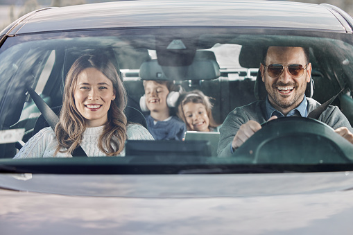Happy parents and their kids enjoying while going on a trip by car. The view is through glass.