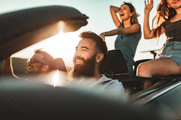 Group of carefree friends having fun while traveling in convertible car during summer day.
