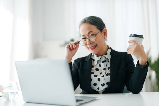 istock Successful Asian senior businessman sitting working with laptop computer and holding coffee in office. 2101030043