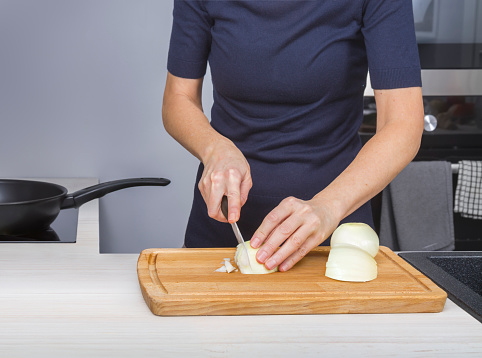 A woman cuts onions on a chopping board for stewing in her kitchen