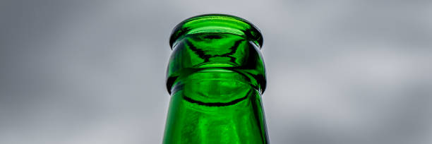 印象的なローアングルショットは、曇り空を背景にした空の緑色のビール瓶のボトルネックを提示し、魅惑的なコントラストを生み出し、創造的なコピーやデザイン要素のための十分な余地� - refundable ストックフォトと画像